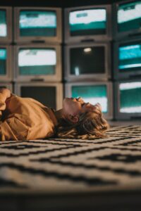 woman staring at ceiling with TV screens in background